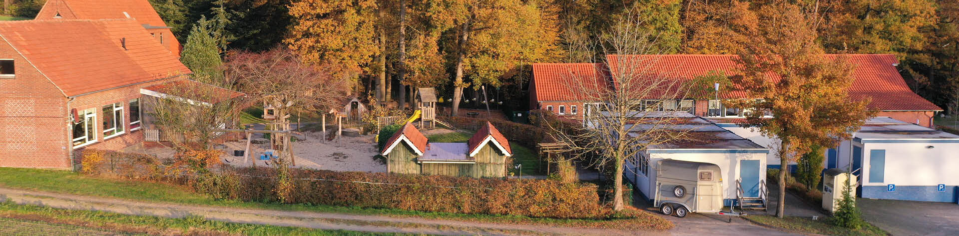 Luftbildaufnahme der Kindertagesstätte Pusteblume mit roten Ziegeldächern neben einem Spielplatz, in einer ländlichen Umgebung.