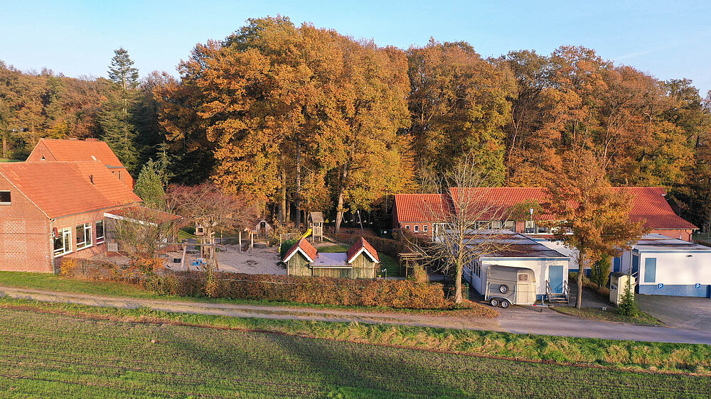 Luftbildaufnahme der Kindertagesstätte Pusteblume mit roten Ziegeldächern neben einem Spielplatz, in einer ländlichen Umgebung.