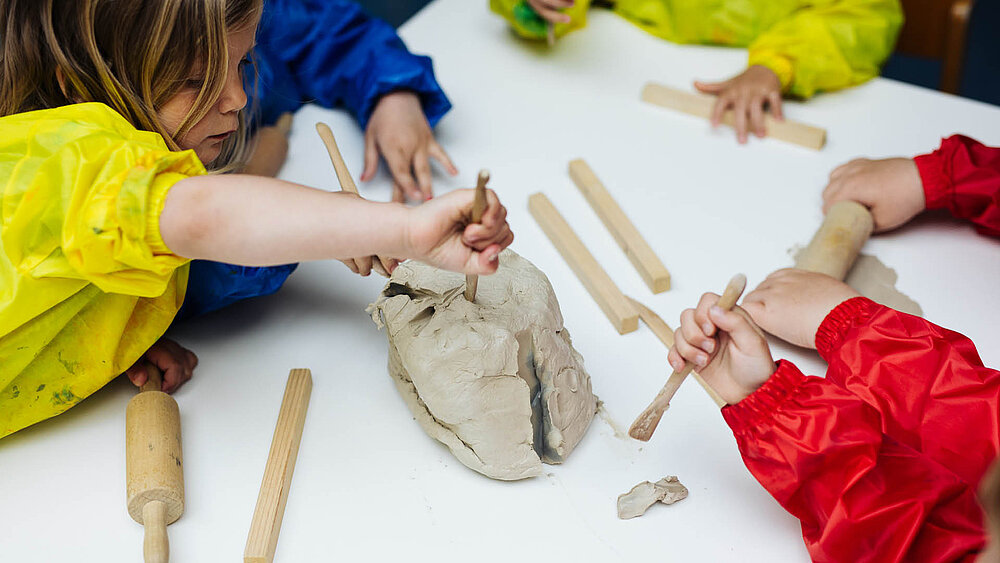 Mehrere Kinder sitzen an einem Tisch und basteln etwas aus Ton.