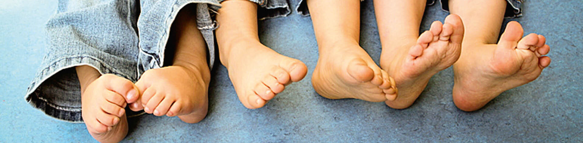 Füße von drei Kindern in Jeans sitzend auf einem Boden. 