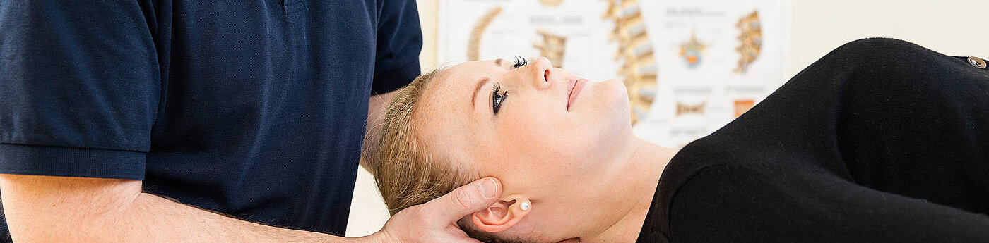 Physiotherapeut behandelt eine Frau am Hinterkopf, die auf dem Rücken liegt.
